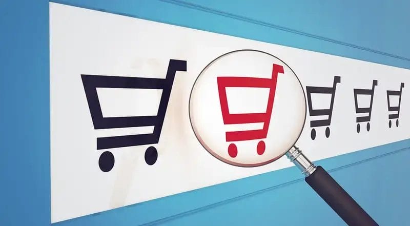 Magnifying glass highlighting a red shopping cart among black icons, symbolizing a comparison of vendors to buy solar eclipse glasses in Spain.